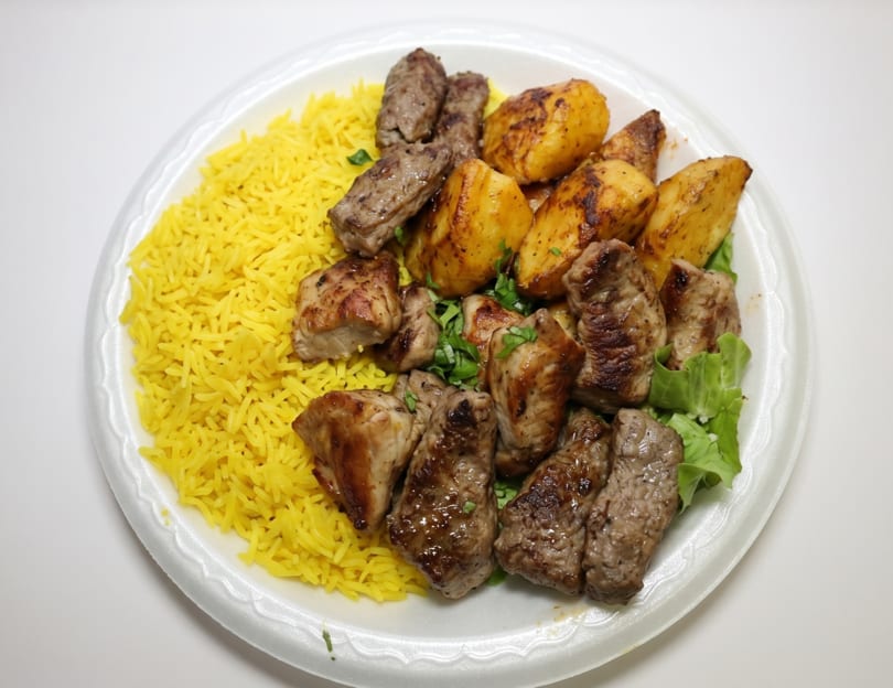 A white plate with yellow rice, roasted potatoes, and various grilled meats, garnished with parsley.