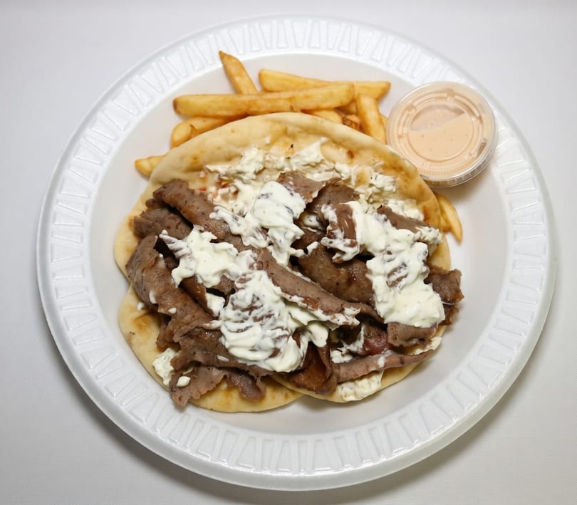 Gyro meat and tzatziki sauce on pita bread with a side of french fries and dipping sauce.