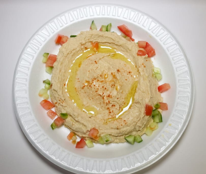 Creamy hummus drizzled with olive oil and sprinkled with paprika, garnished with diced tomatoes and cucumbers.