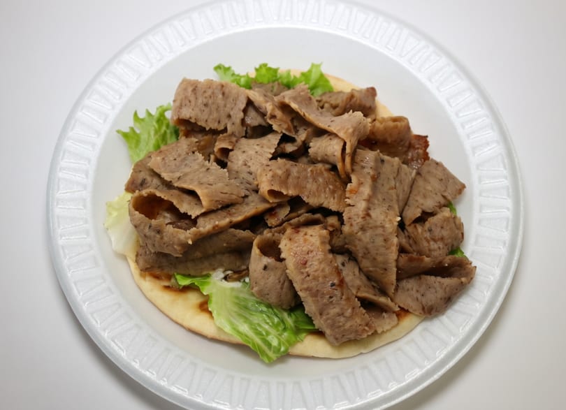 Gyro meat and lettuce on pita bread, served on a white disposable plate.