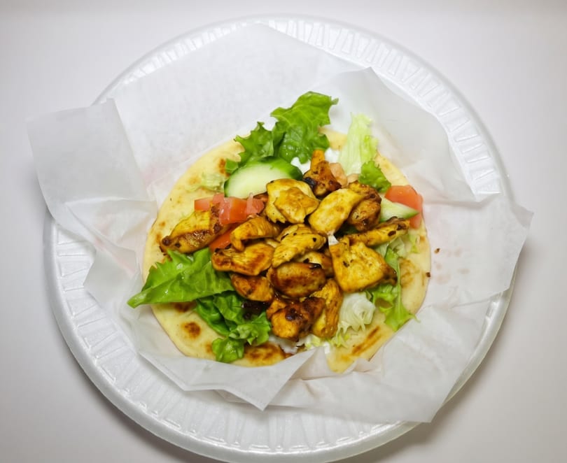 Chicken shawarma pita with lettuce, tomatoes, and cucumbers on a white plate.