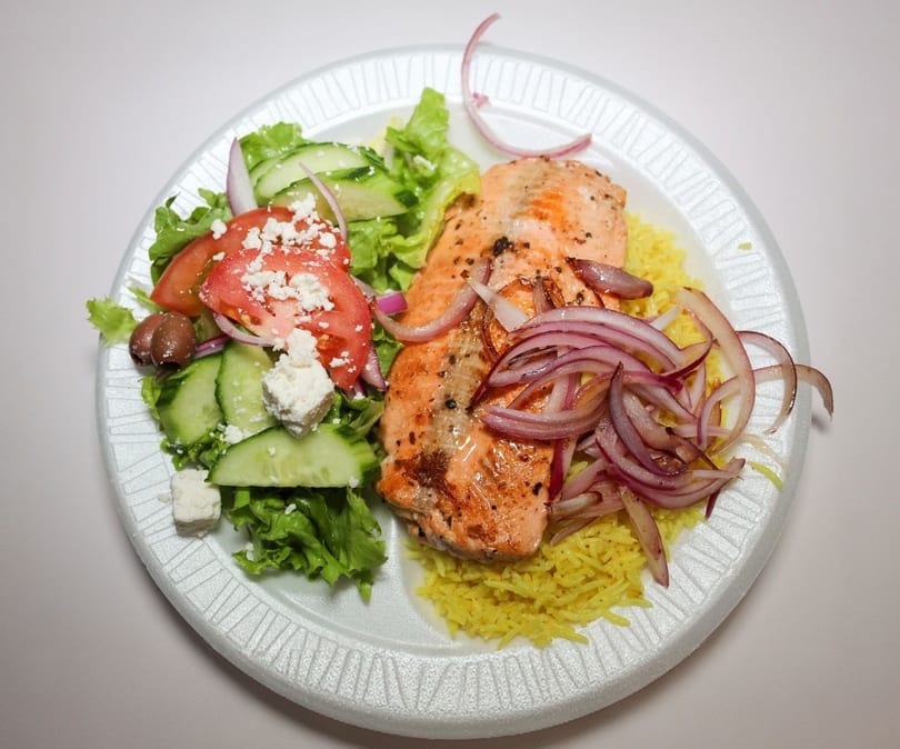 Grilled salmon with red onions, yellow rice, and a side salad with feta cheese and olives.